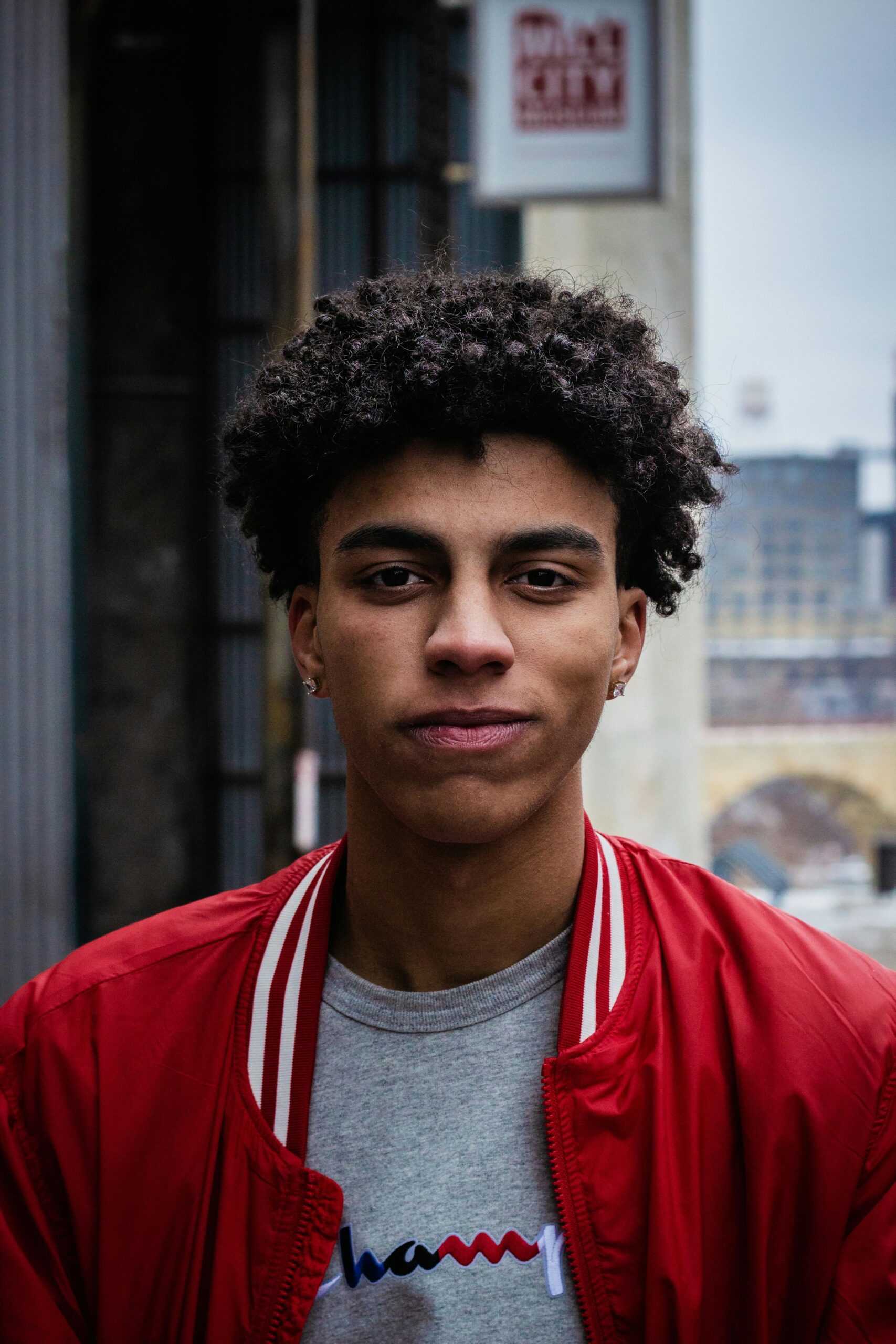 Our Team Portrait of a young man in a red jacket, captured in an urban setting with a solemn expression.