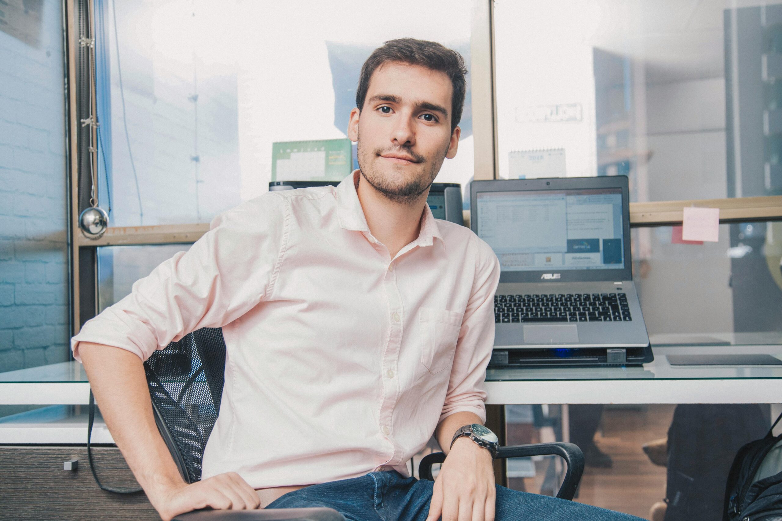 Our Team Confident young man in shirt working in modern office with laptop and desk accessories.